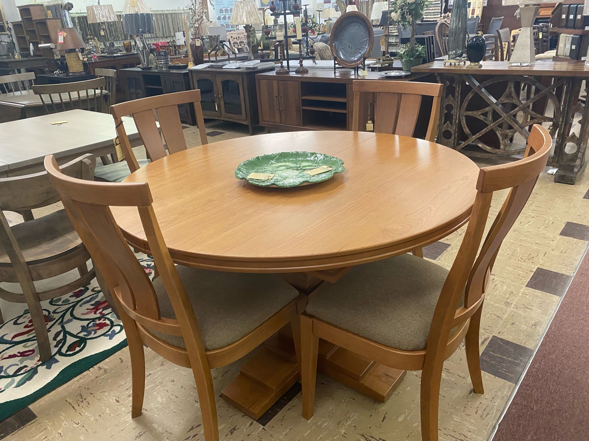 A round wooden dining table with four matching chairs featuring beige upholstered seats, placed in a furniture store.