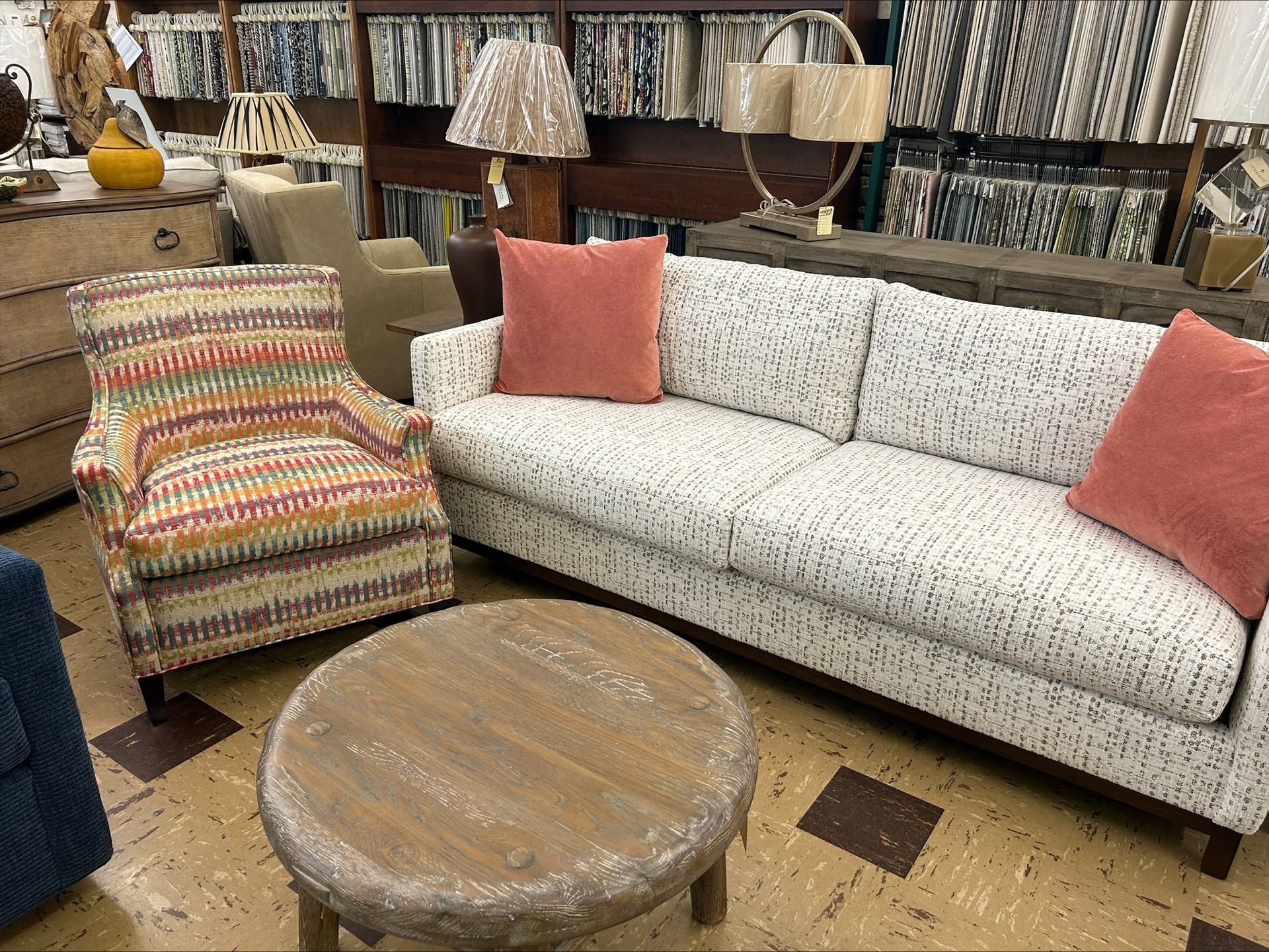 A furniture store display featuring a striped patterned armchair, a light patterned sofa with coral pillows, and a table.