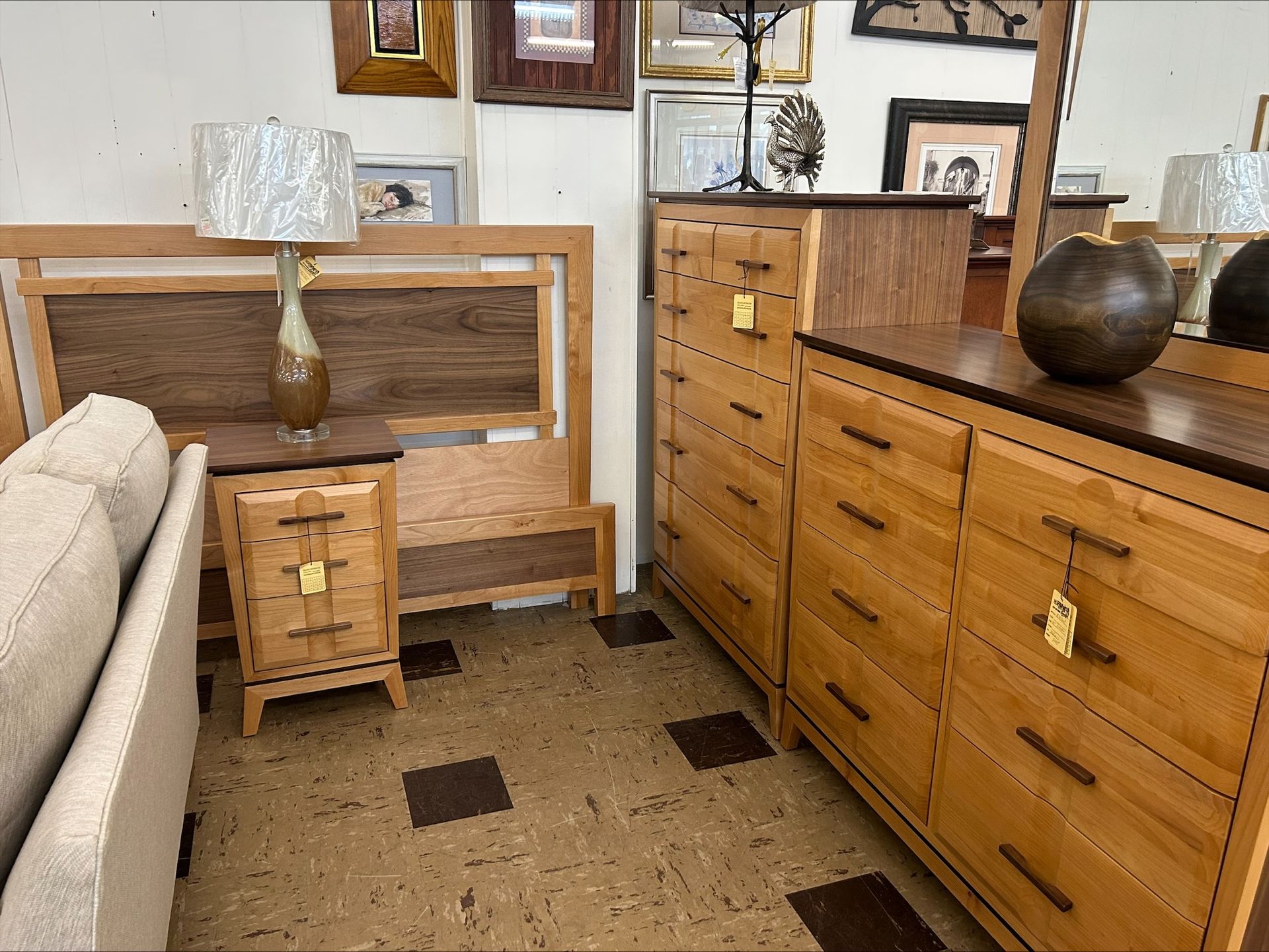 A store showroom featuring light wood bedroom furniture, including a headboard, nightstand, dresser, and chest of drawers.