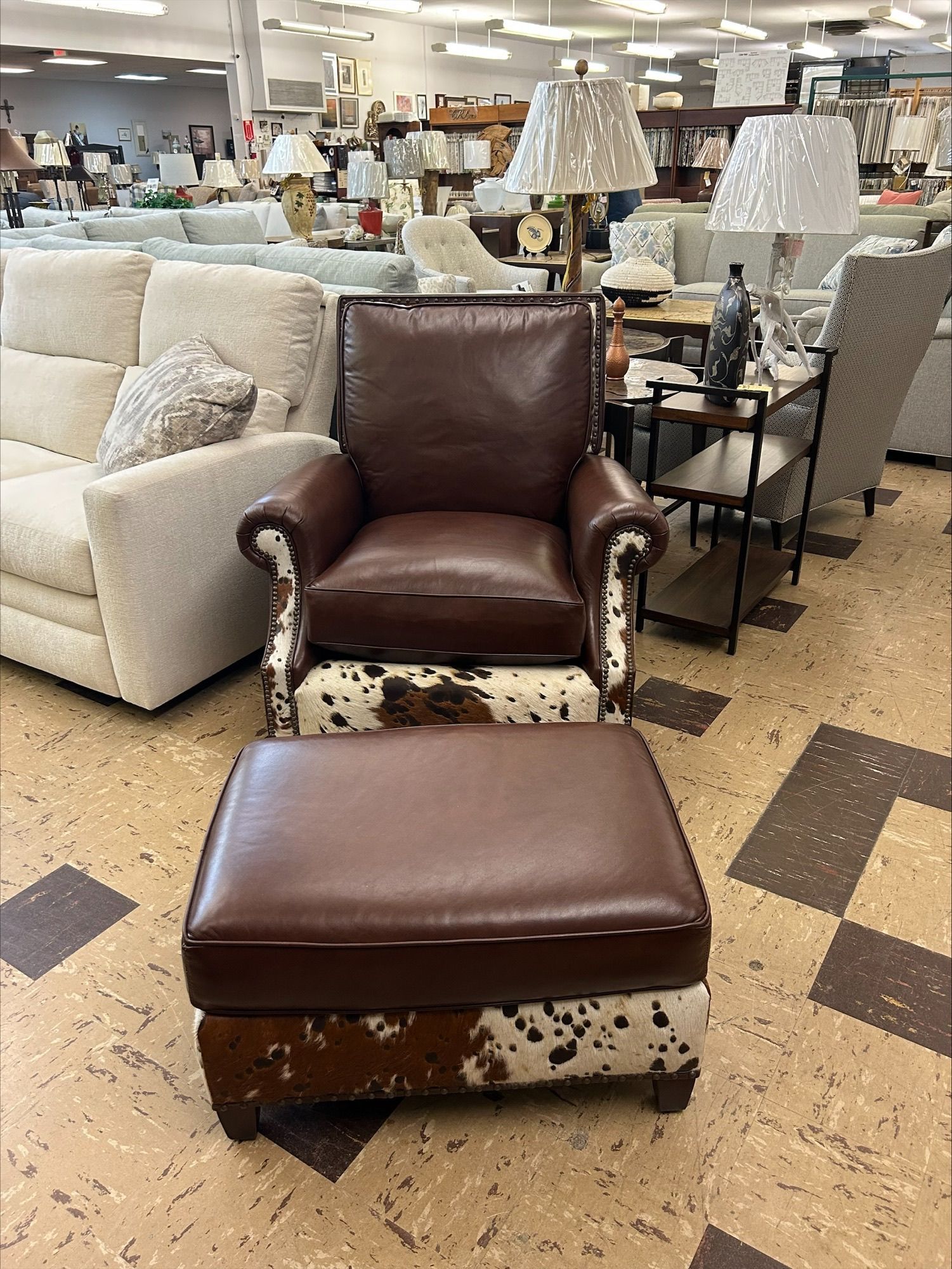 A brown leather armchair with cowhide accents and a matching ottoman displayed in a furniture store.