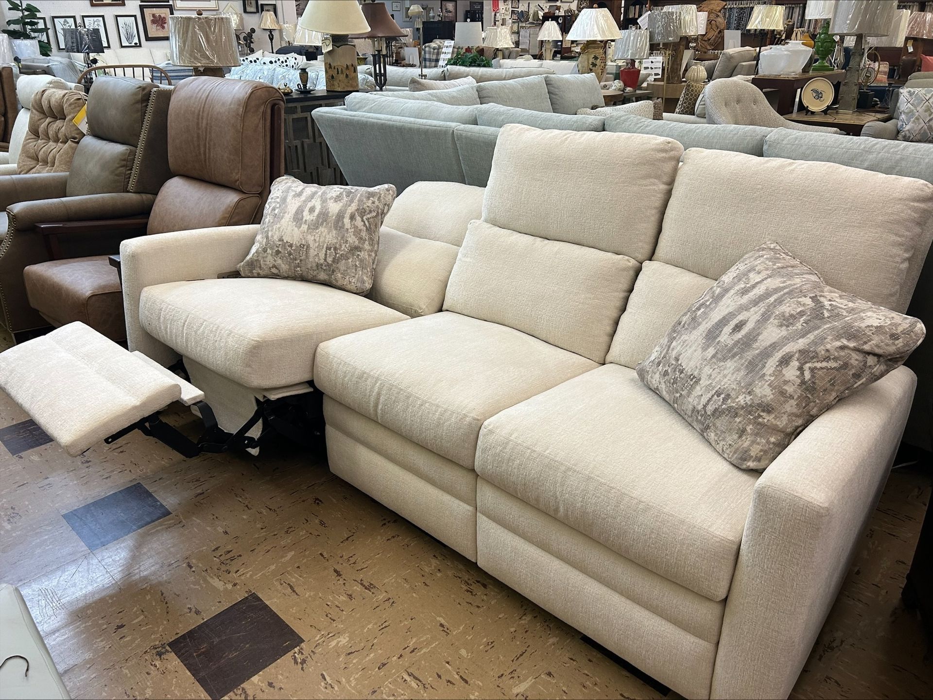 A cream-colored, multi-seat reclining sofa with decorative patterned throw pillows, displayed in a furniture showroom.