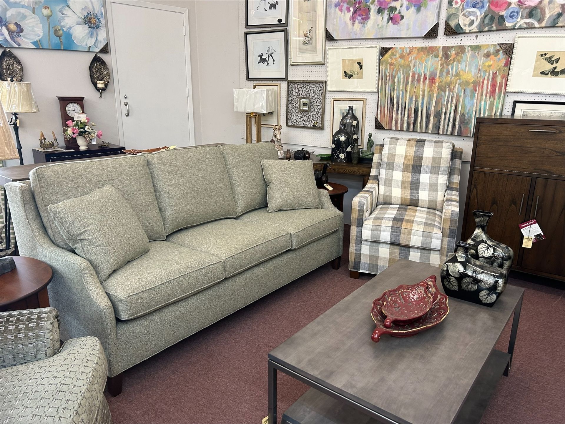 A furniture showroom displays a gray patterned sofa, a plaid armchair, a wooden cabinet, and a gray coffee table.