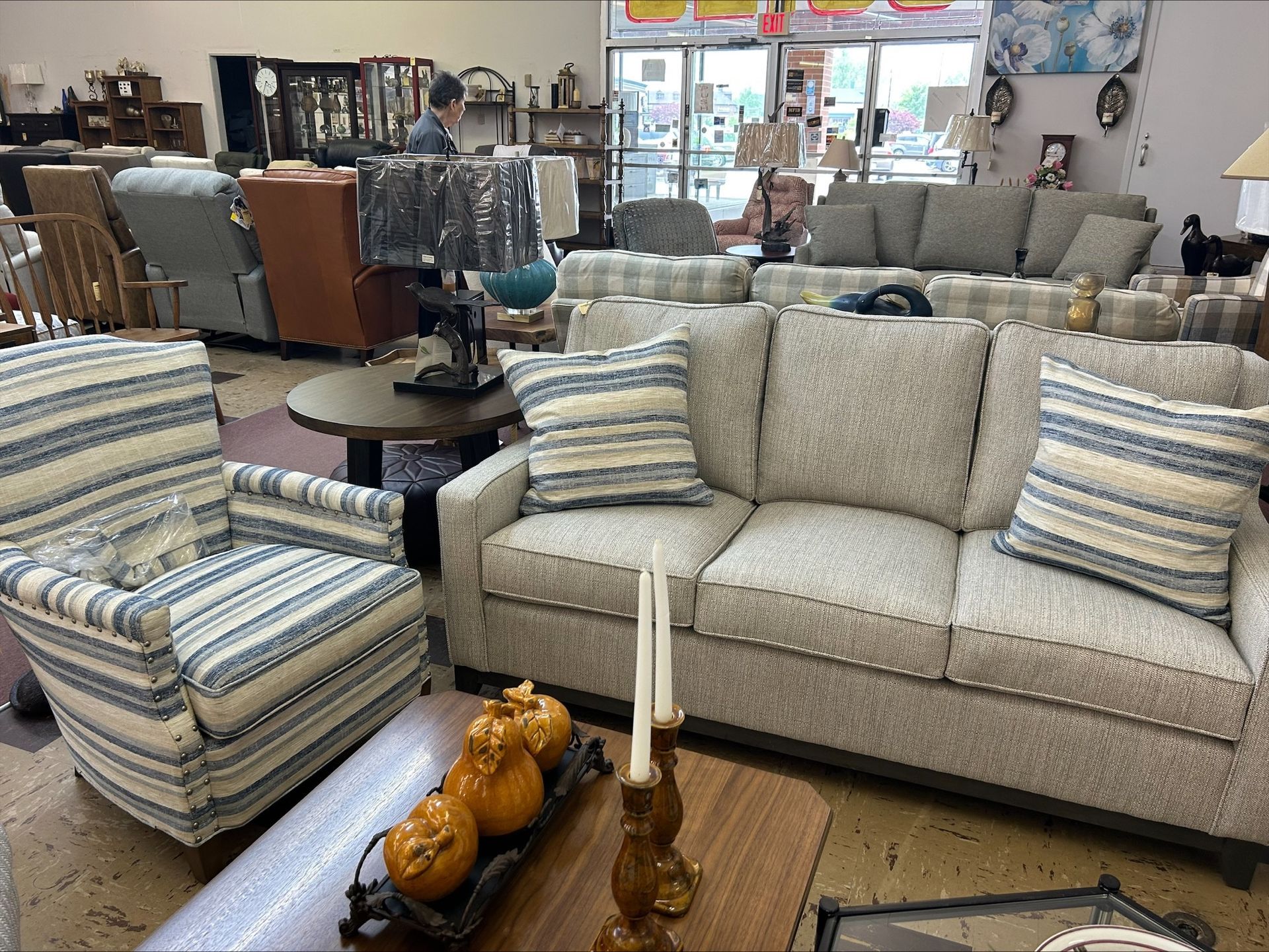 A furniture store showroom featuring a striped armchair, a light-colored couch with matching pillows, and decor on tables.