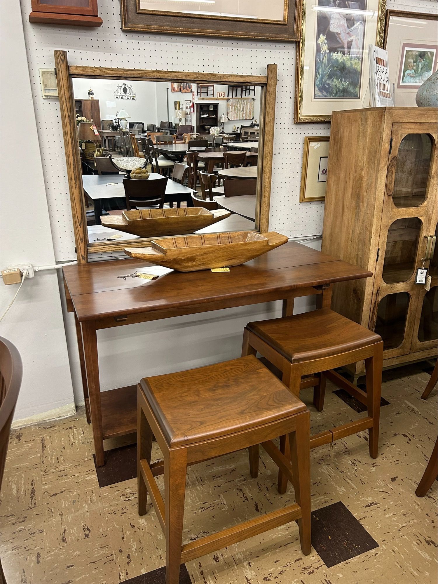 A rustic wood vanity set with a mirror, console table, and two matching wooden stools in a retail store.