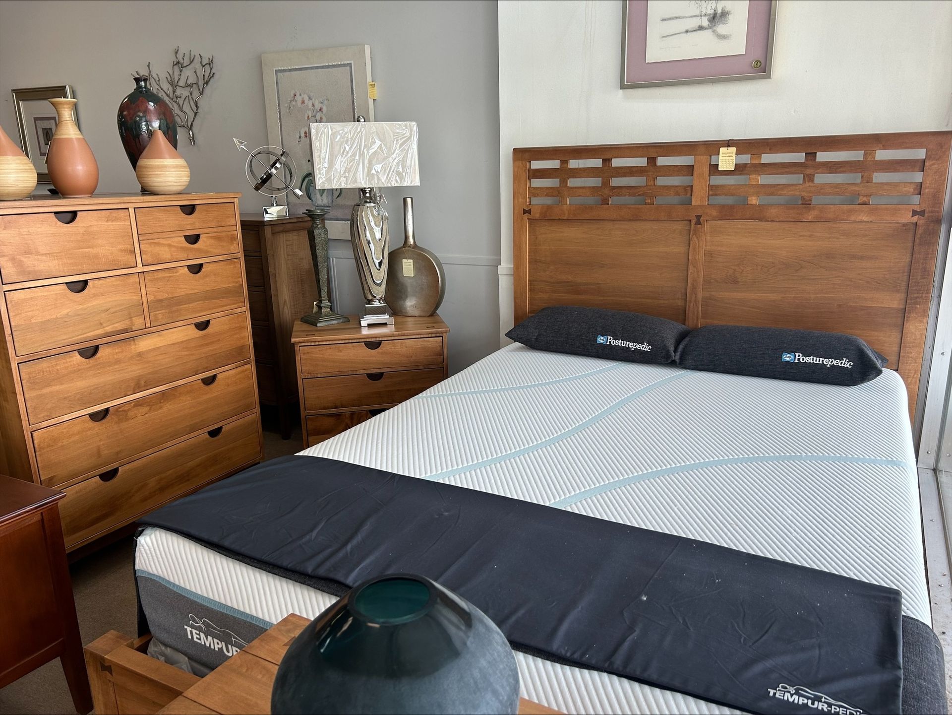 A wood bedroom set featuring a headboard, dresser, and nightstand with a mattress topped with a dark runner and pillows.