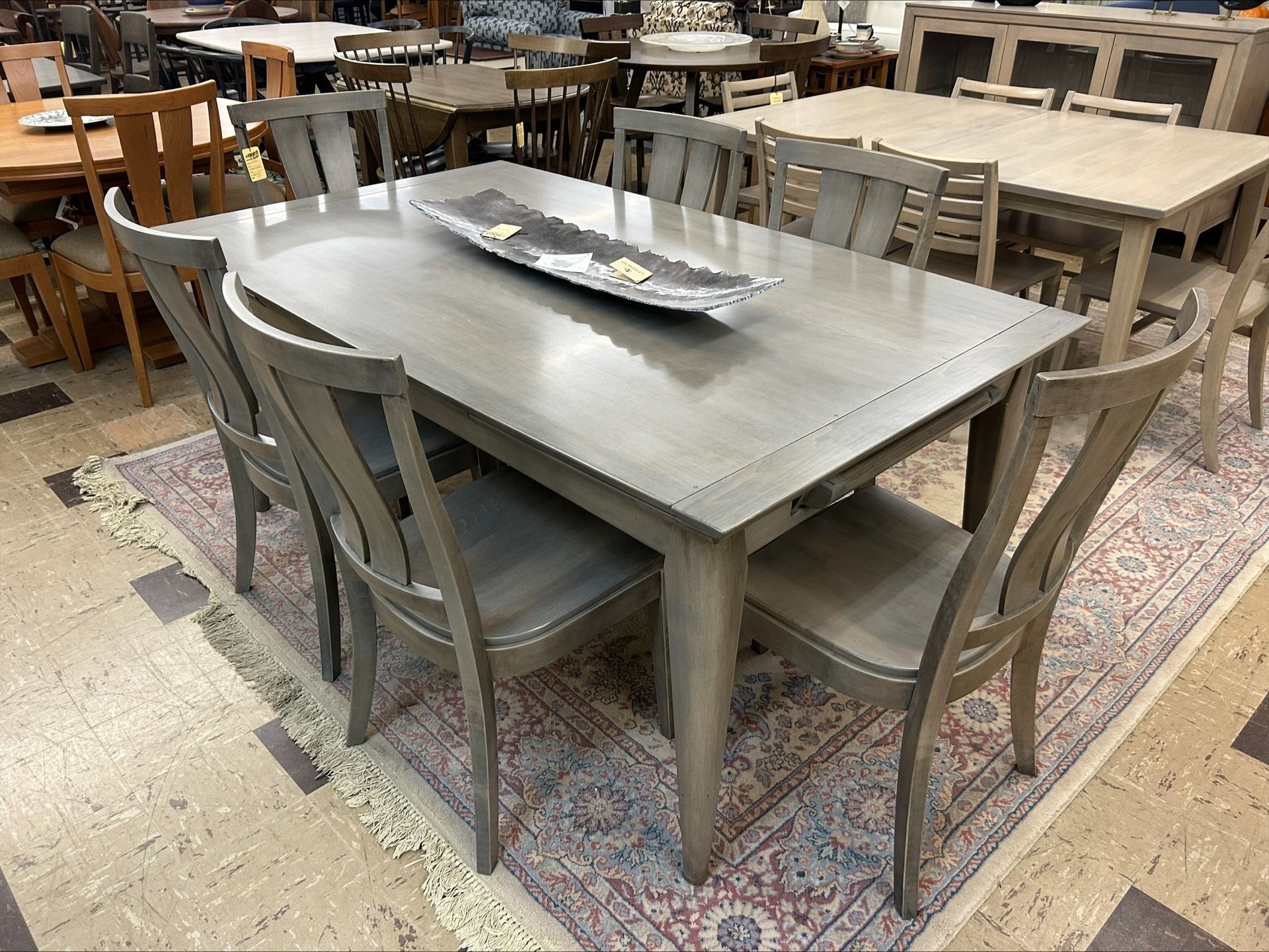 A gray wooden dining table set with chairs on a patterned rug in a furniture showroom.