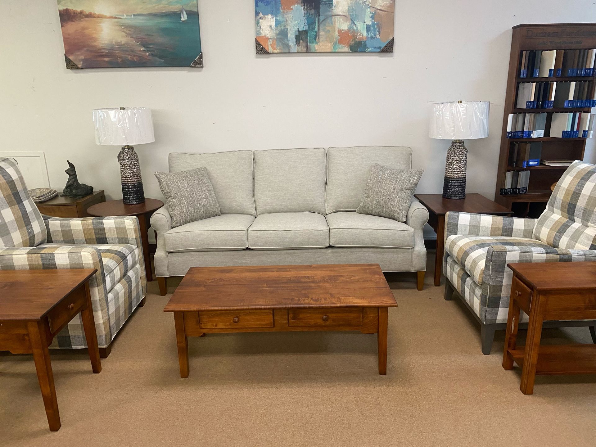 A living room set with a light-colored sofa, two plaid armchairs, a wooden coffee table, end tables, lamps, and a bookcase.
