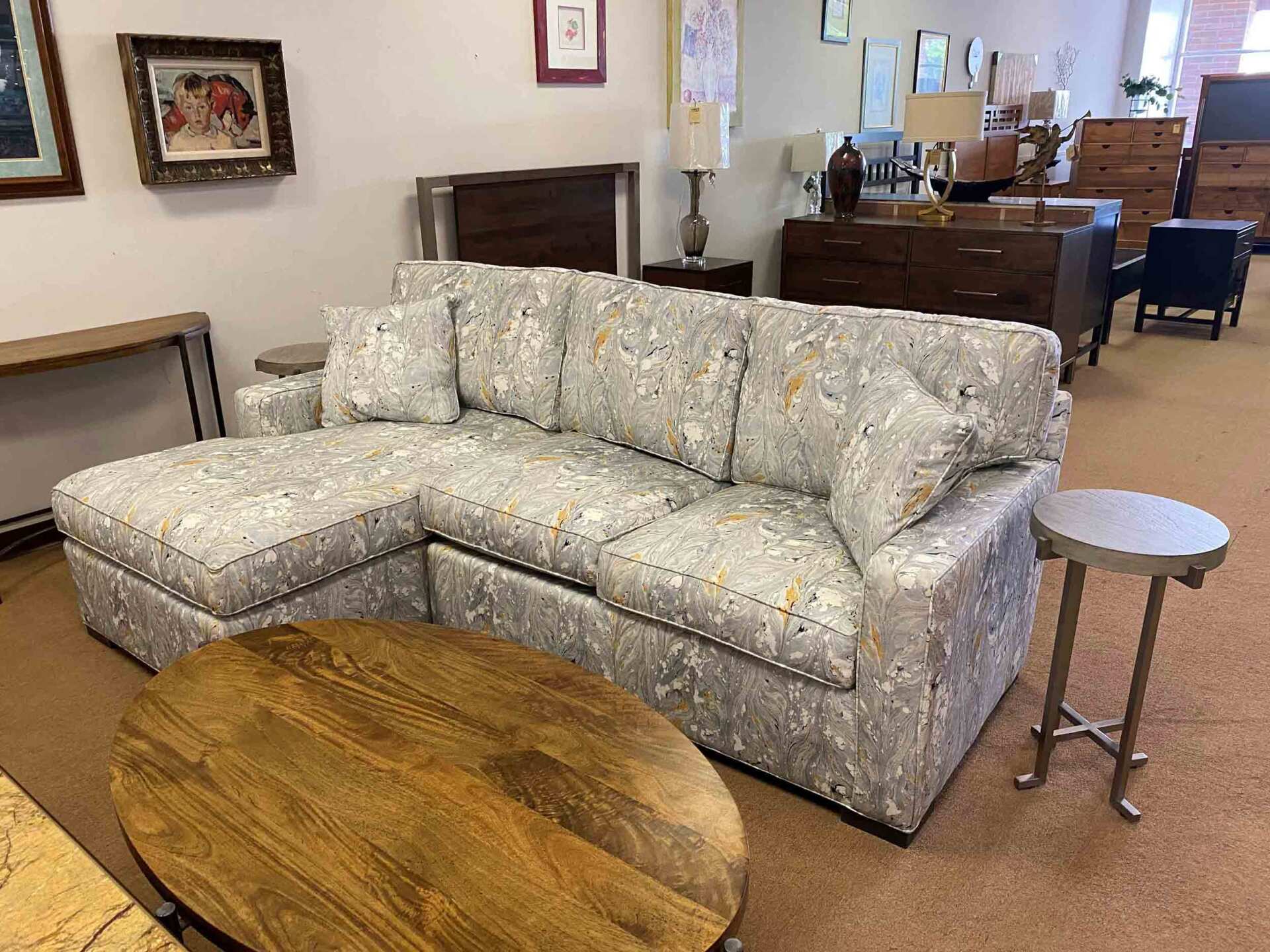 A floral patterned sectional sofa with a chaise in a showroom setting, accompanied by a round wooden coffee table.