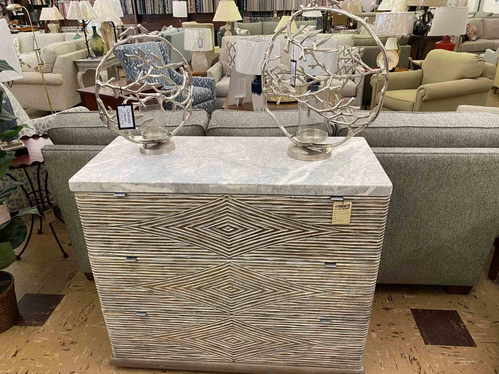 A chest with a marble top and wood-textured geometric patterns, featuring two circular metal sculptures on display.