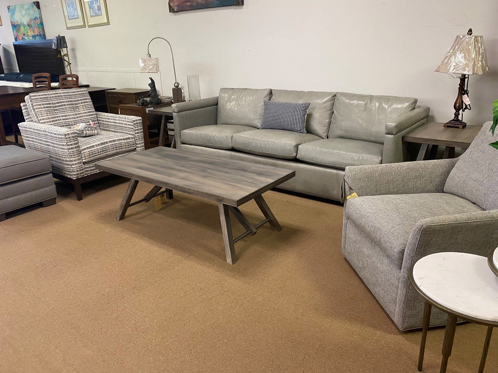 A living room furniture display featuring a grey sofa, patterned armchairs, a wooden coffee table, and lamps.