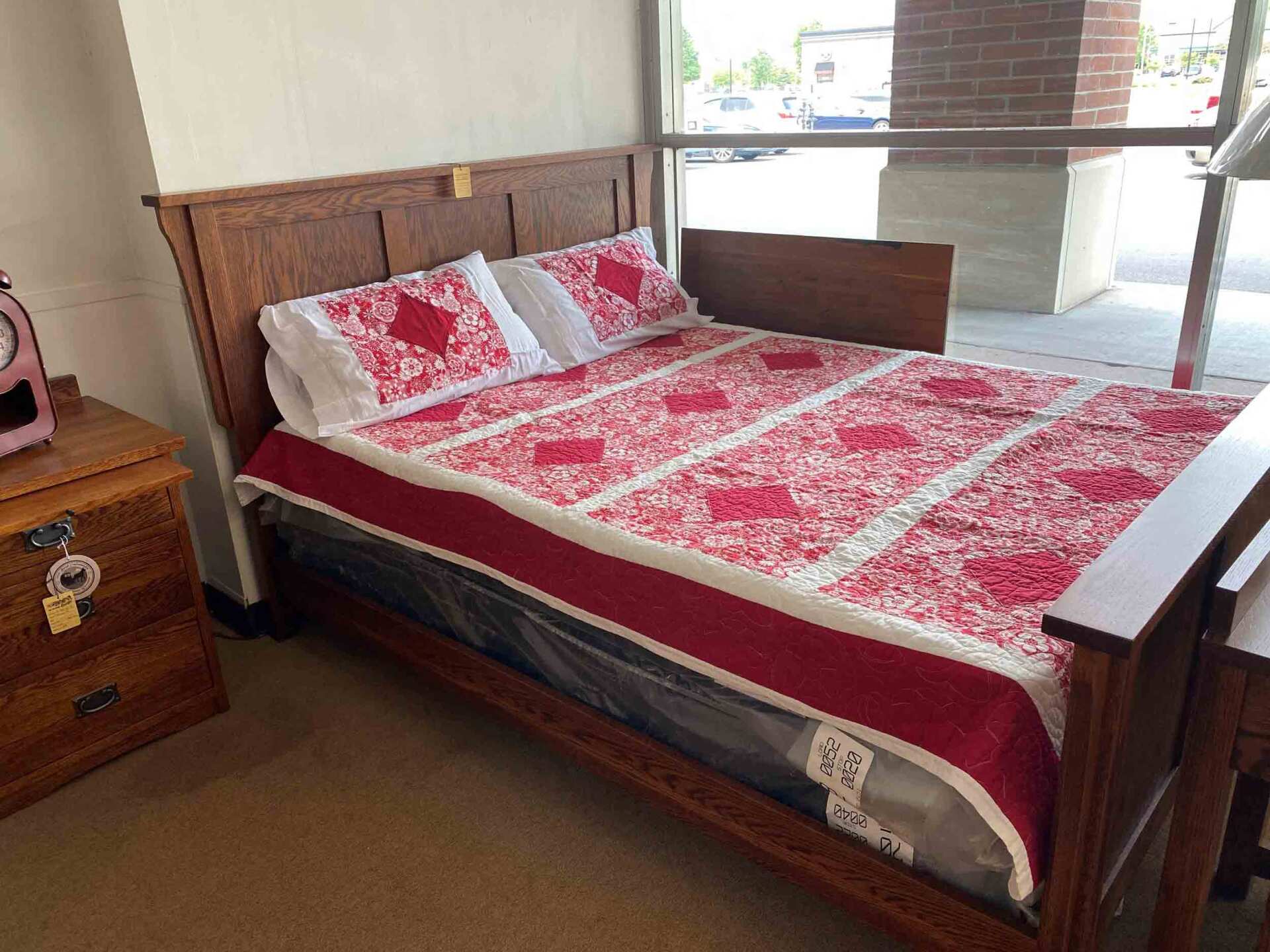 A wooden bed frame with a red and white patterned quilt and pillows in a room near a window.