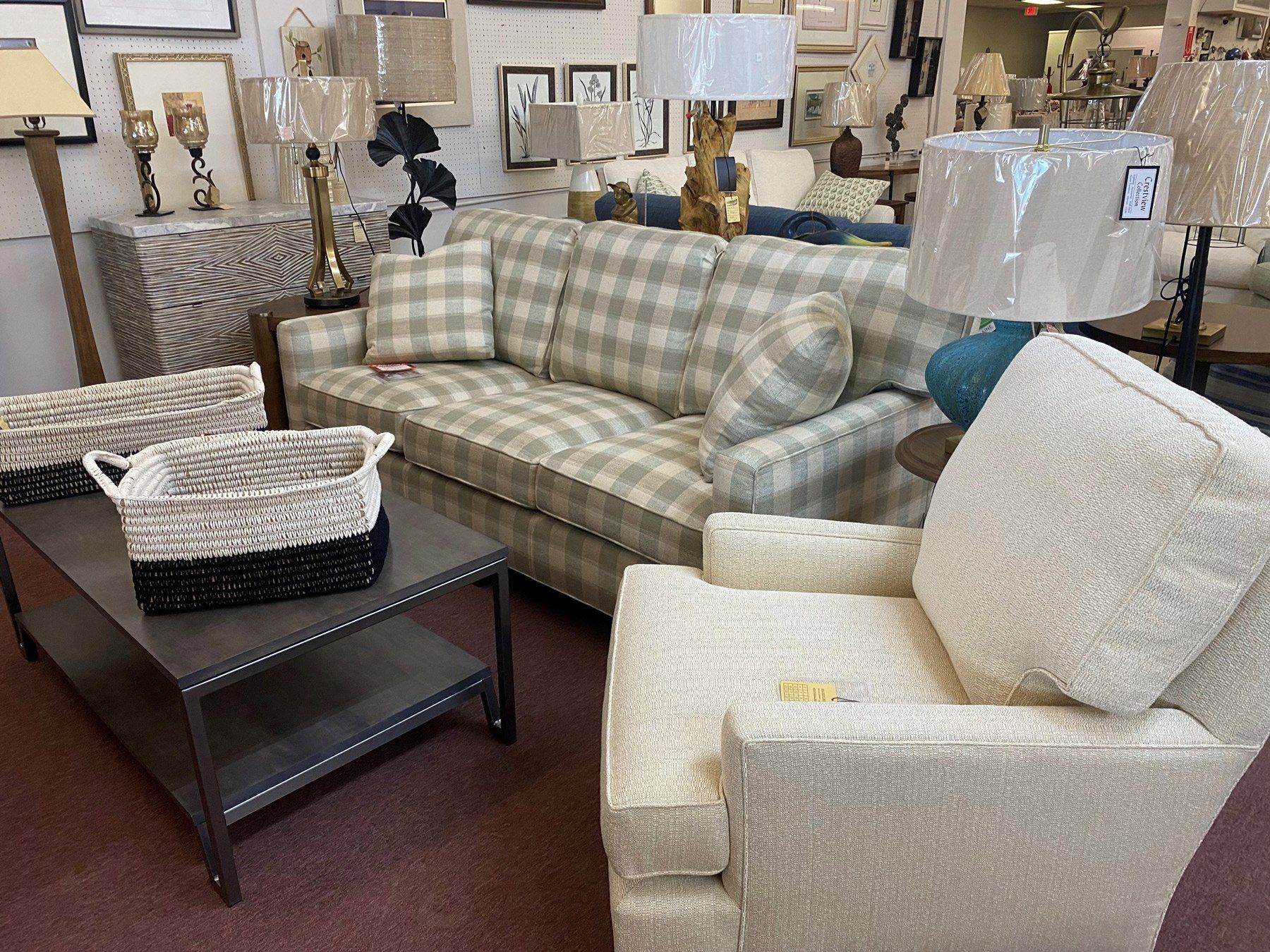 A plaid sofa, a textured cream armchair, and a dark coffee table with a two-toned basket in a furniture showroom.