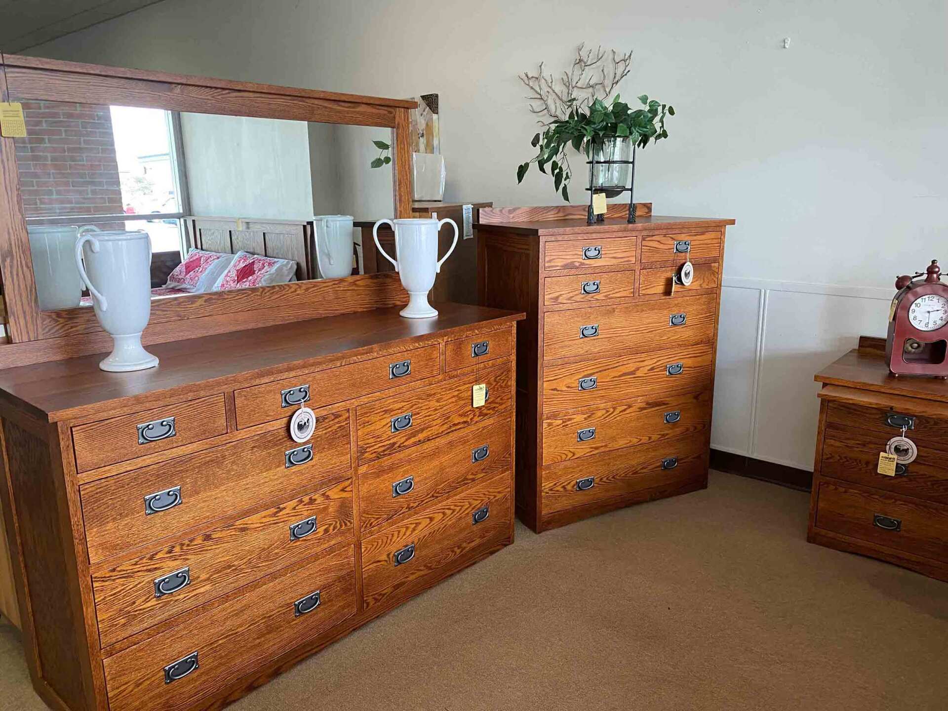 A bedroom set of oak furniture, including a dresser with a mirror, a tall chest, and a nightstand in a retail setting.