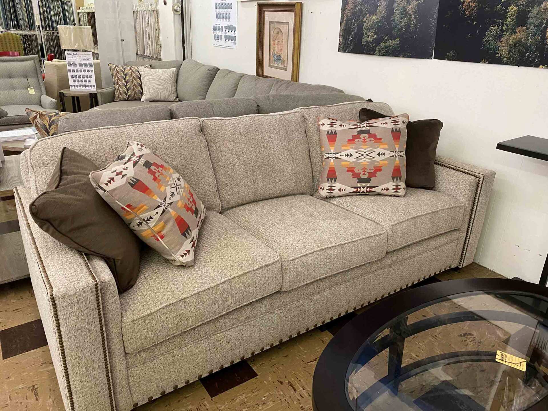 A neutral-colored, textured sofa with decorative patterned and solid brown throw pillows in a furniture store.