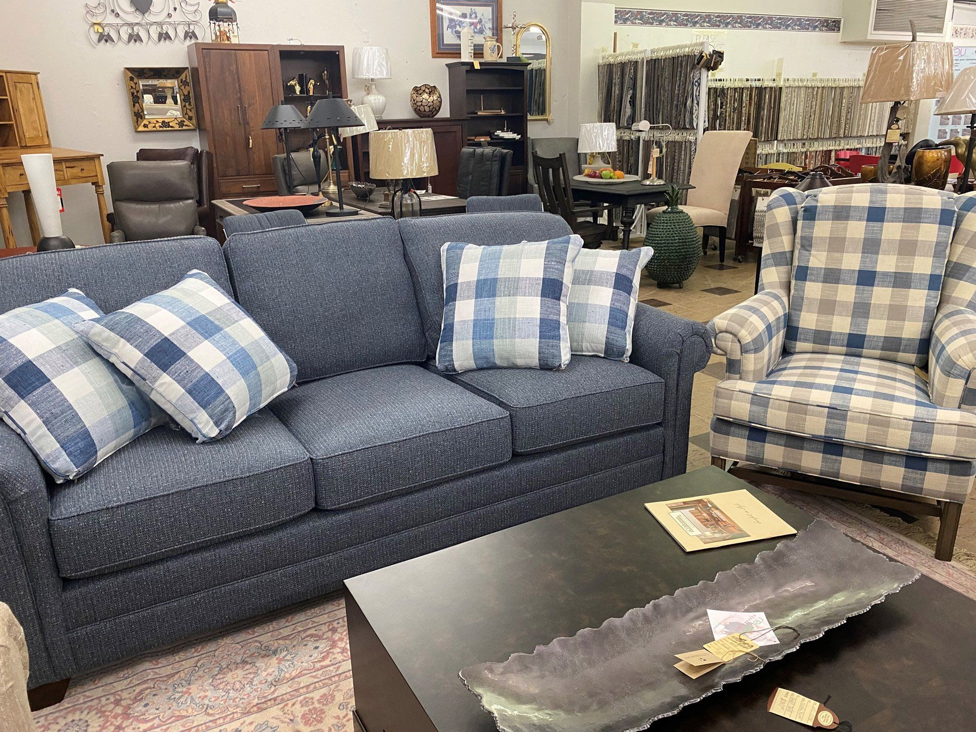 A blue fabric sofa with plaid throw pillows next to a matching plaid armchair in a furniture showroom.