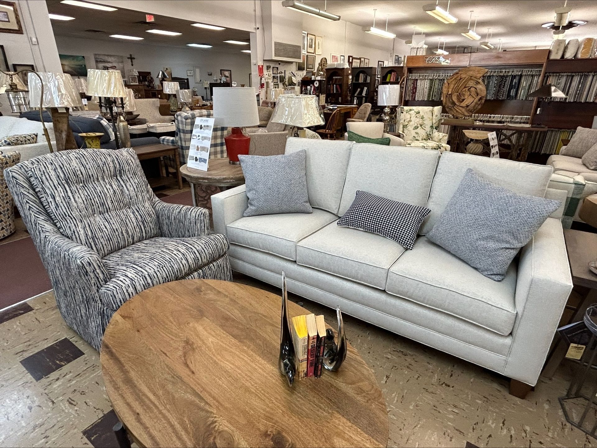 A light-colored sofa with blue accent pillows, a patterned armchair, and a round wooden coffee table in a furniture store.