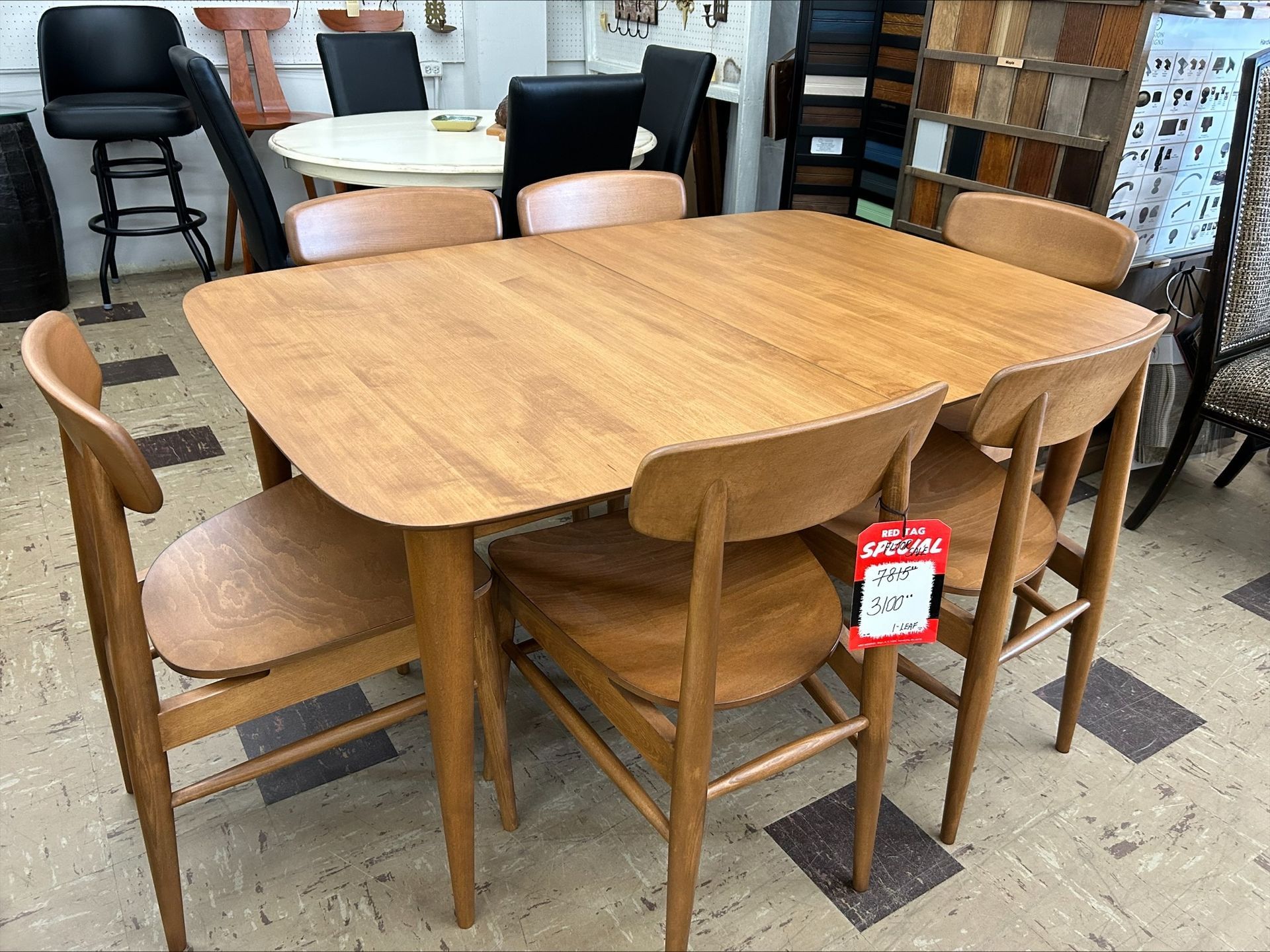 A wooden dining table with rounded corners surrounded by four matching wooden chairs in a furniture showroom.