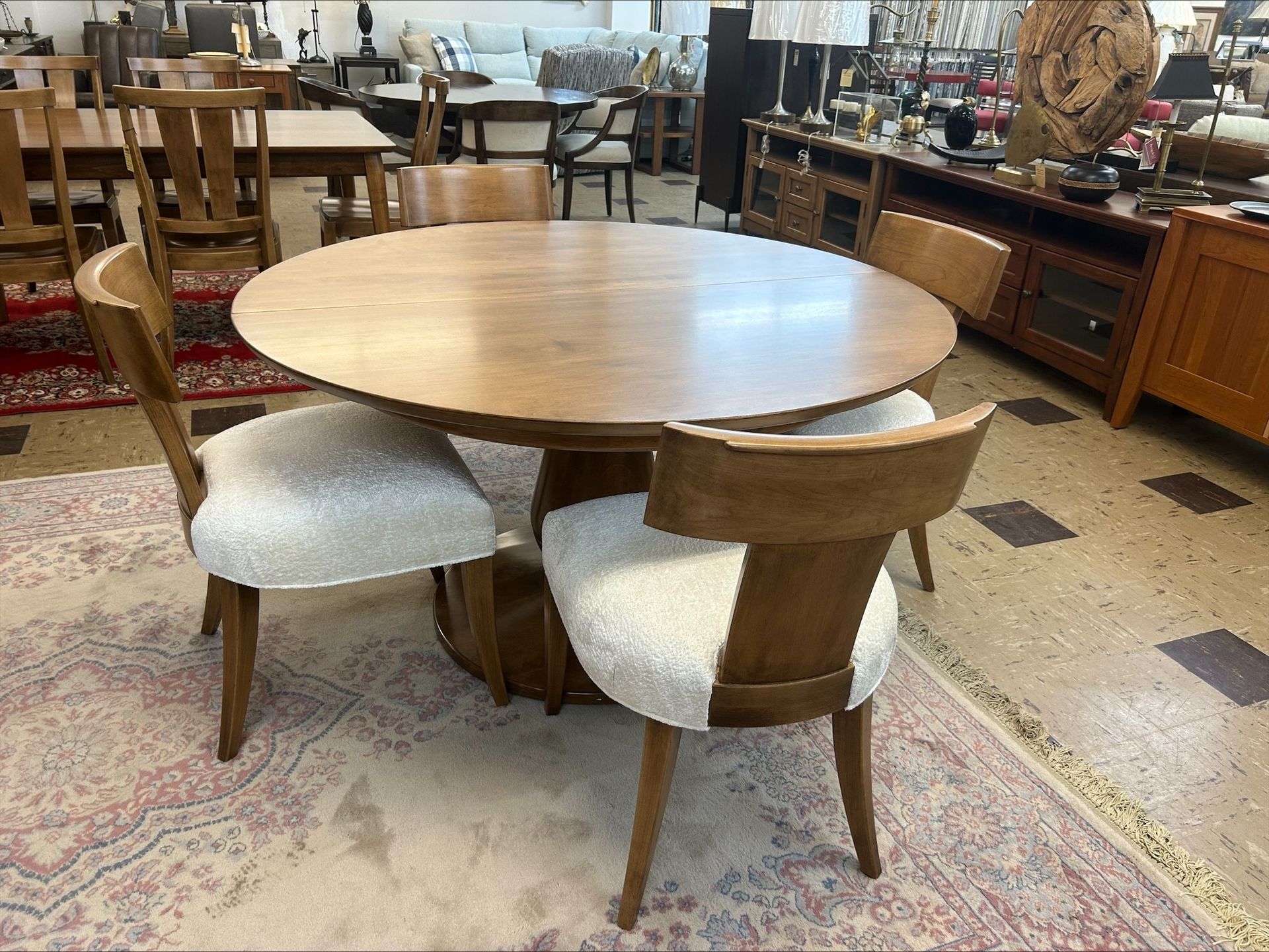 Round wooden dining table with four upholstered chairs in a furniture showroom