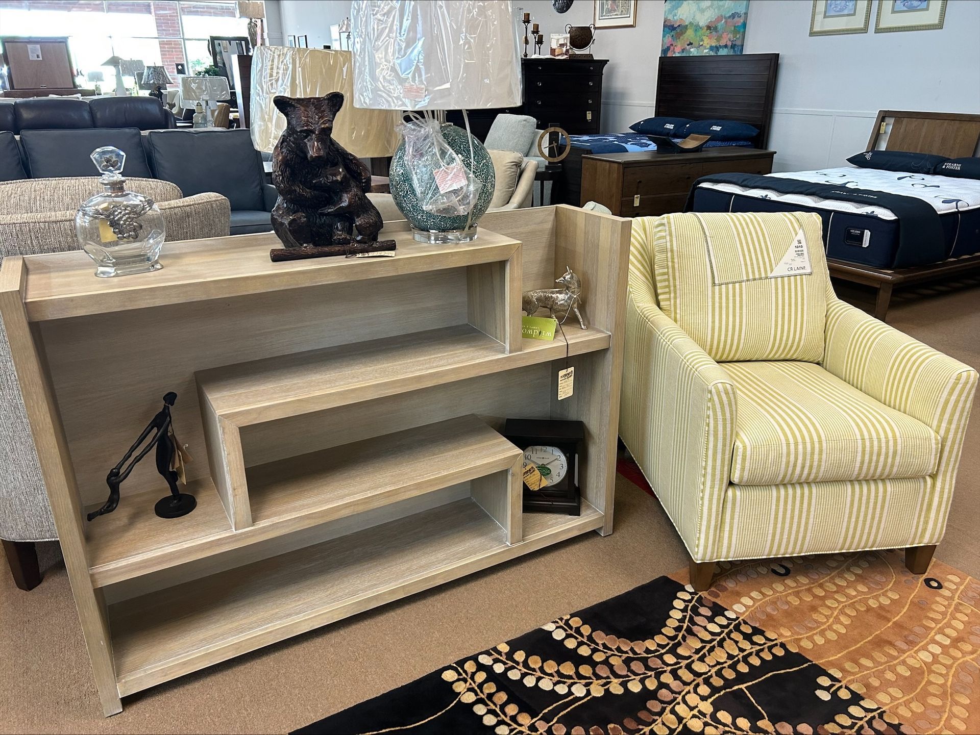 A light wood open-shelf display unit, a beige striped armchair, and decor in a furniture showroom.
