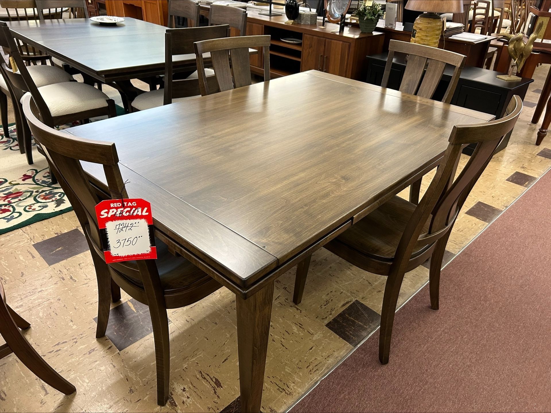 A brown wooden dining table with matching chairs arranged in a furniture store showroom.