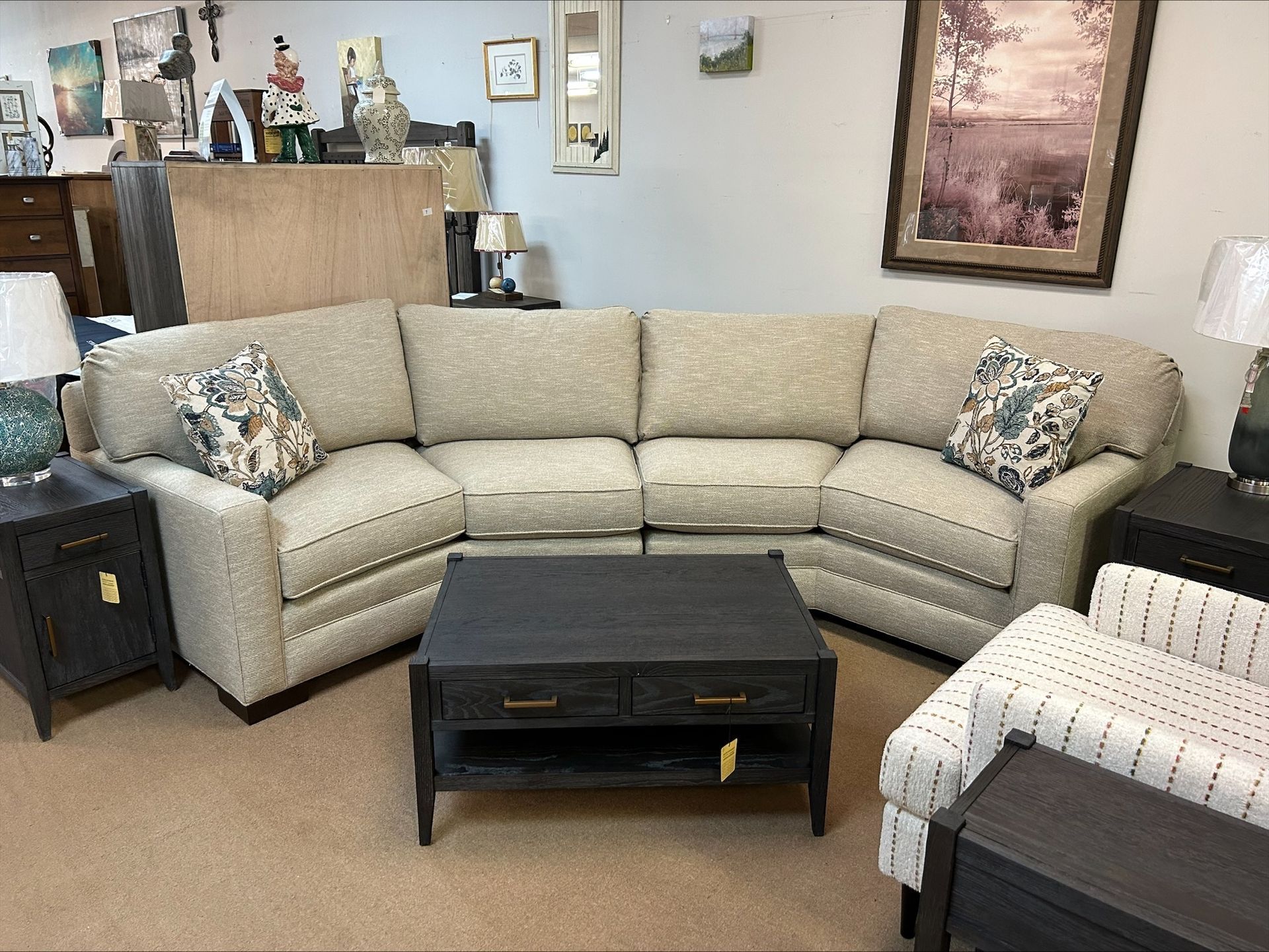A curved, beige fabric sectional sofa with patterned throw pillows, centered around a dark wooden coffee table in a shop.