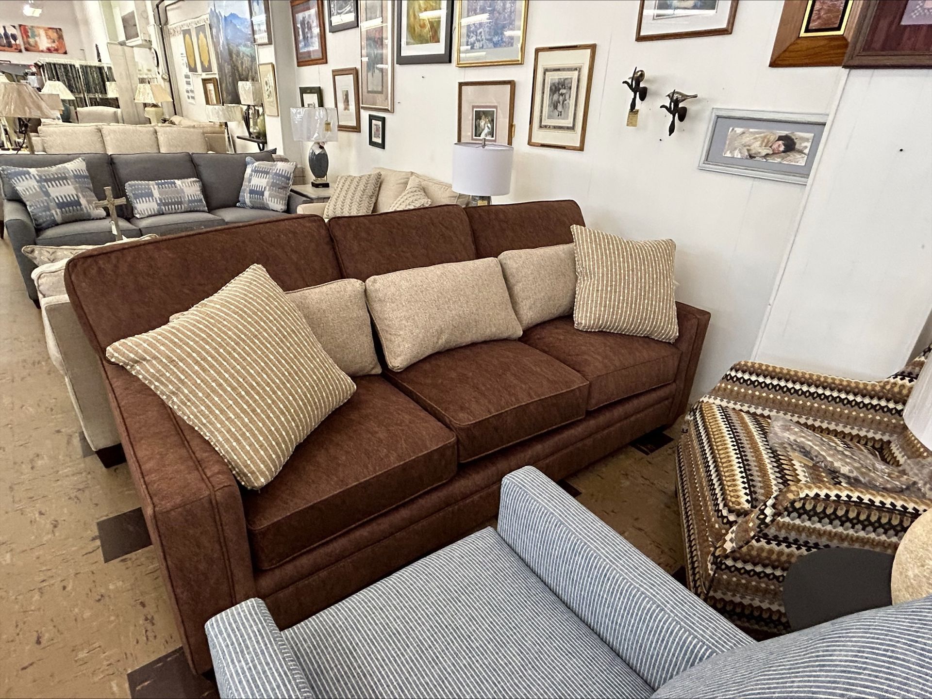 A brown couch with textured throw pillows, a patterned armchair, and a striped accent chair in a furniture showroom.