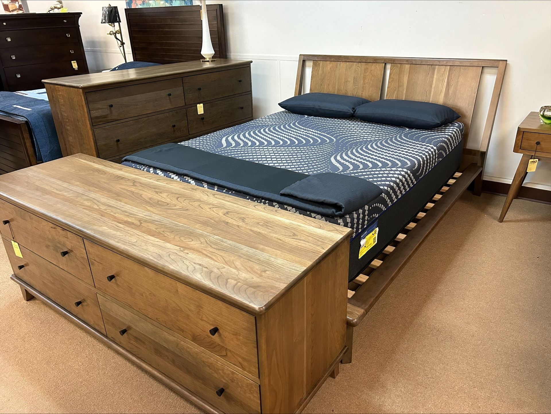A bedroom display featuring a wooden bed frame, matching storage bench, and a dresser in a store showroom.