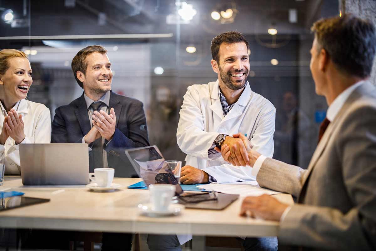 A group of people are sitting around a table shaking hands with a doctor.