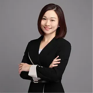 Eva  in a black suit is standing with her arms crossed and smiling.