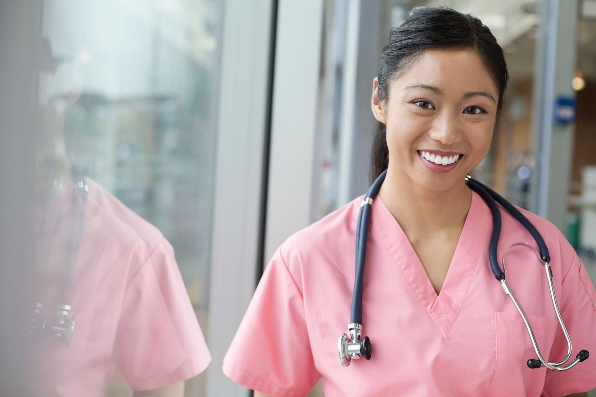 A woman in a pink scrub with a stethoscope around her neck is smiling.