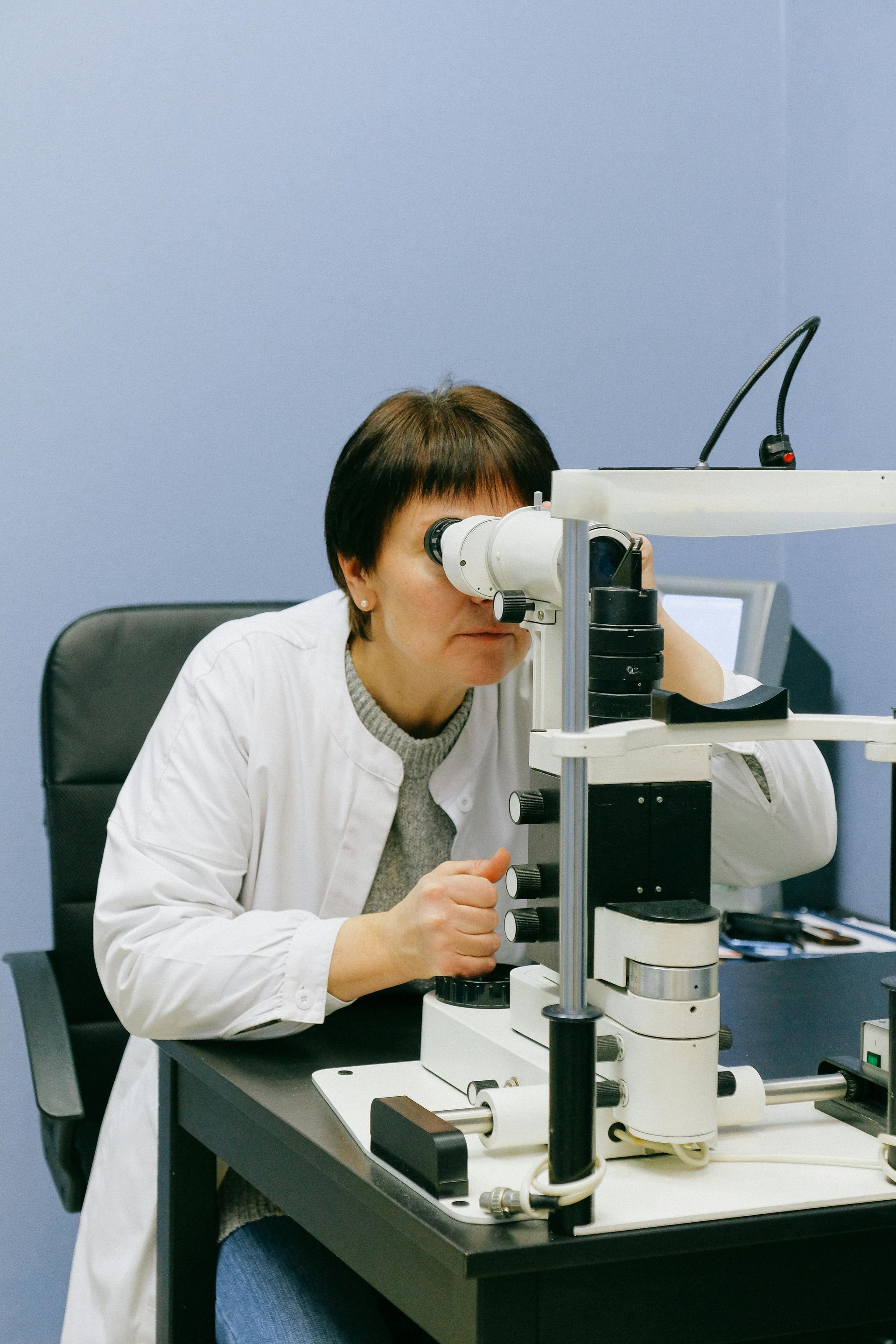 A man wearing glasses and a white coat is standing in front of an eye exam machine.