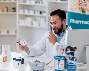 A pharmacist is talking on a cell phone while holding a bottle of pills.