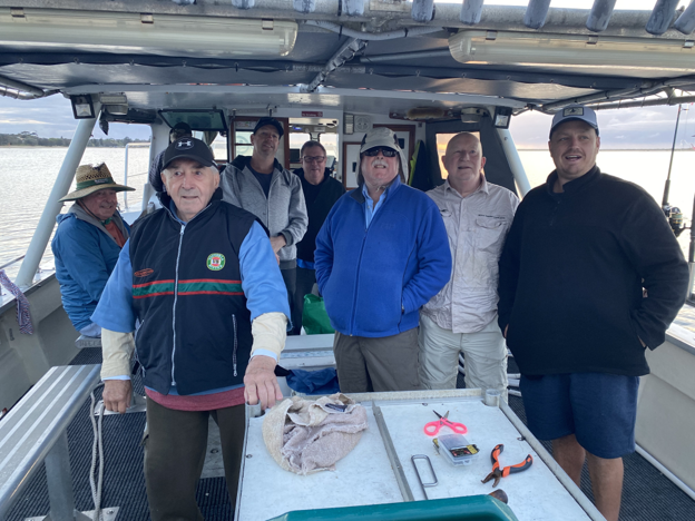 Group of fishing club members standing together on a boat out on water