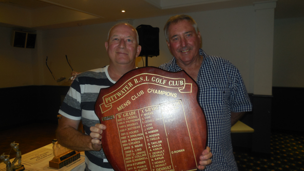 Two men proudly holding a large club championship shield indoors