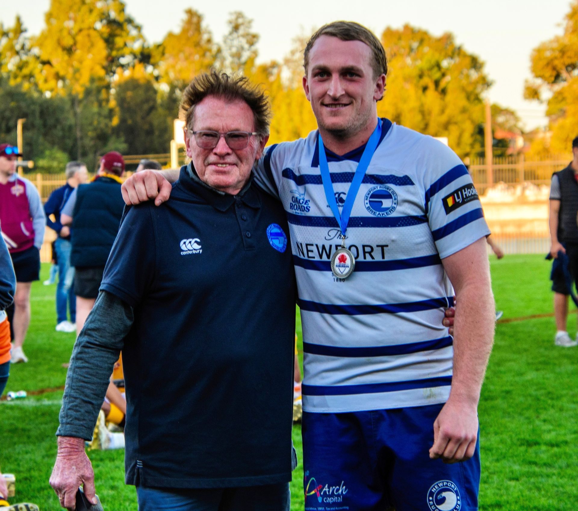 Alan Jones smiling beside a young rugby player wearing a medal on field