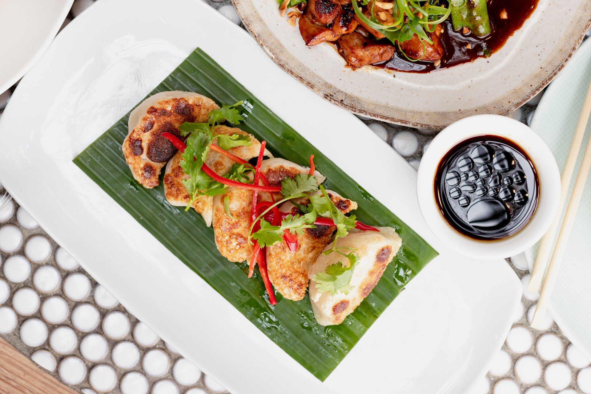 Plated Asian-style dumplings and seafood served on a banana leaf with fresh herbs and dipping sauce at Wok O’clock