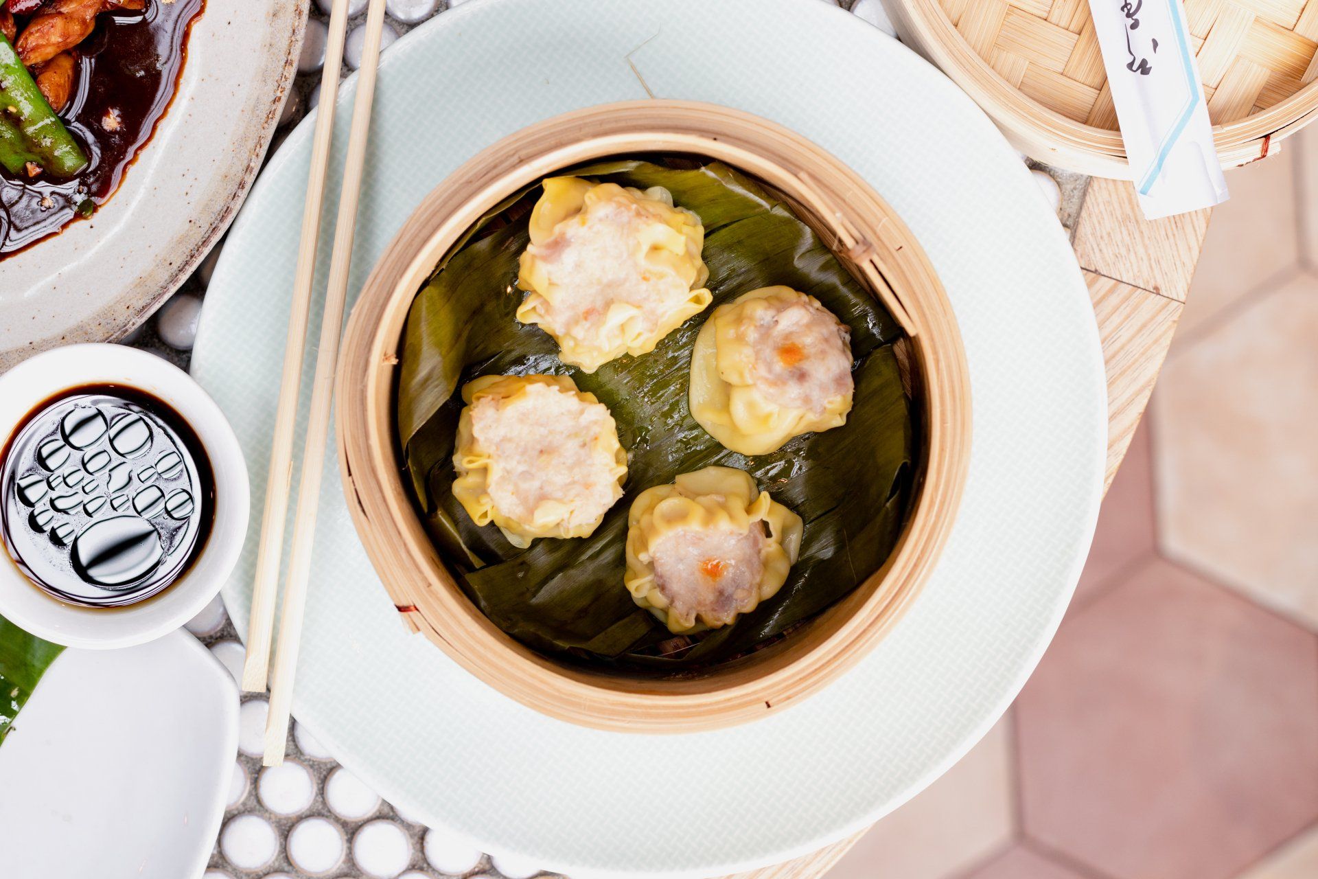 Steamed dumplings in a bamboo basket lined with banana leaf, served with dipping sauce at Wok O’clock