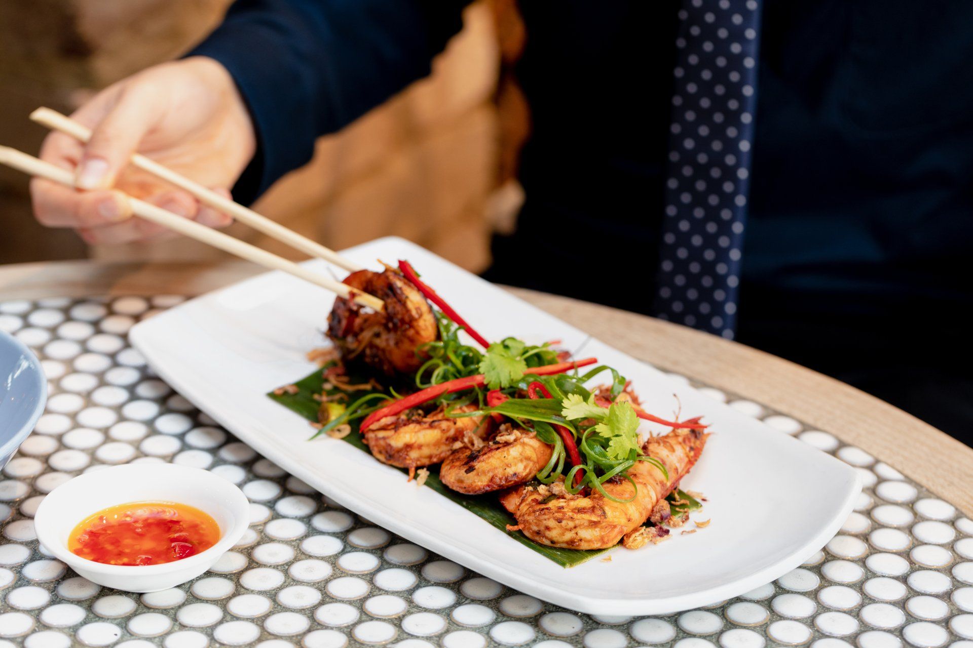 Hand using chopsticks to eat crispy Asian-style dish garnished with herbs at Wok O’clock