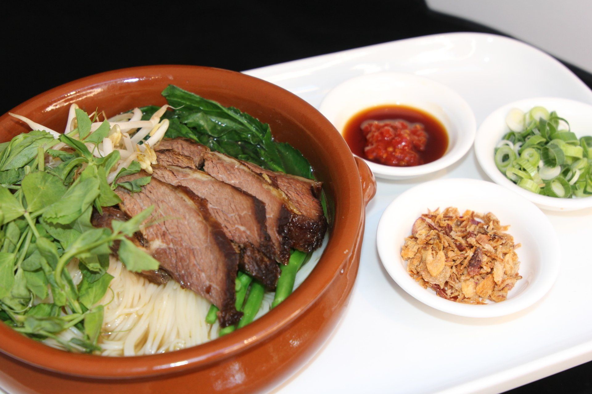 Asian noodle bowl topped with sliced meat, herbs and condiments, served with side sauces