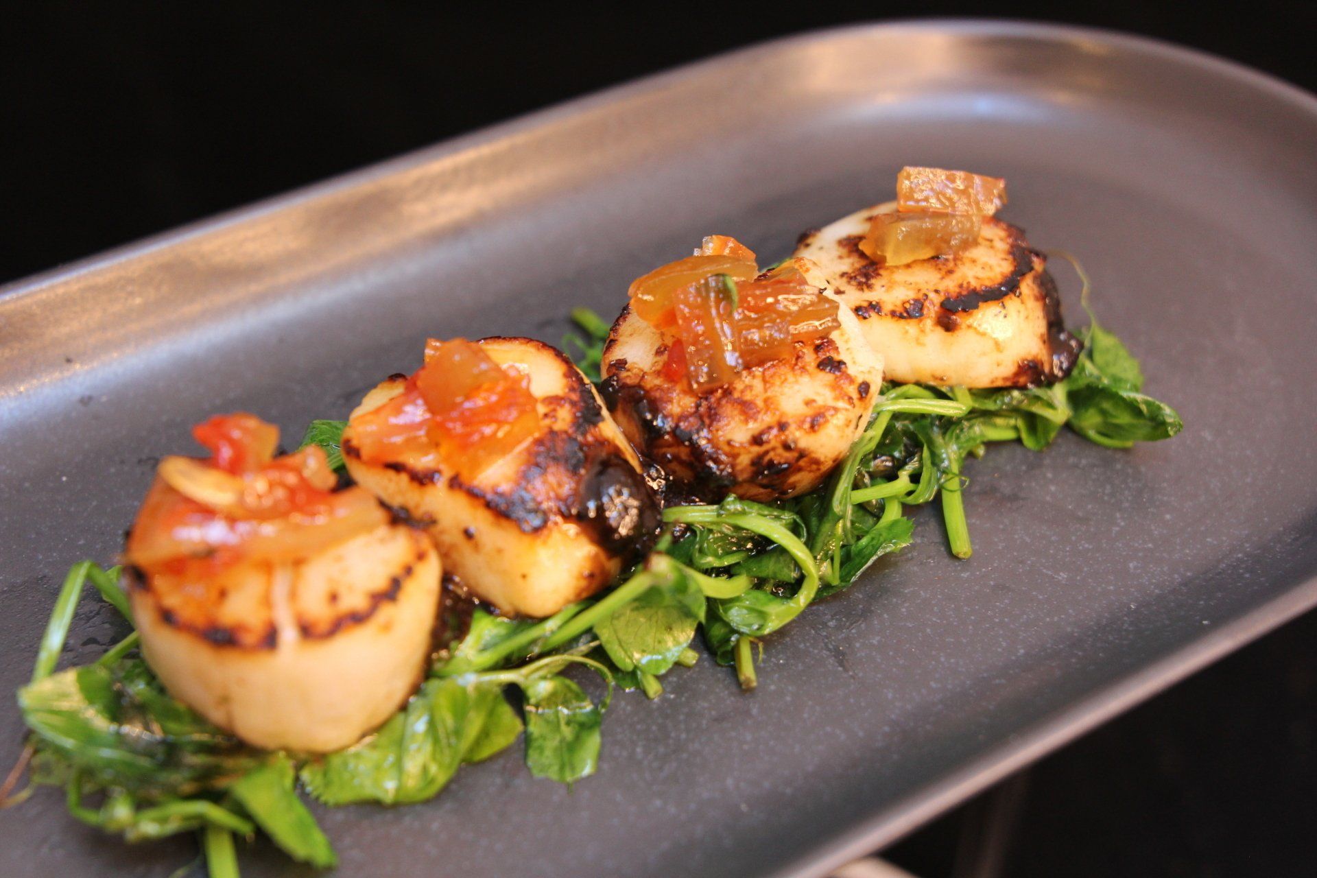 Seared scallops glazed in sauce, served on greens on a rectangular plate at Wok O’clock