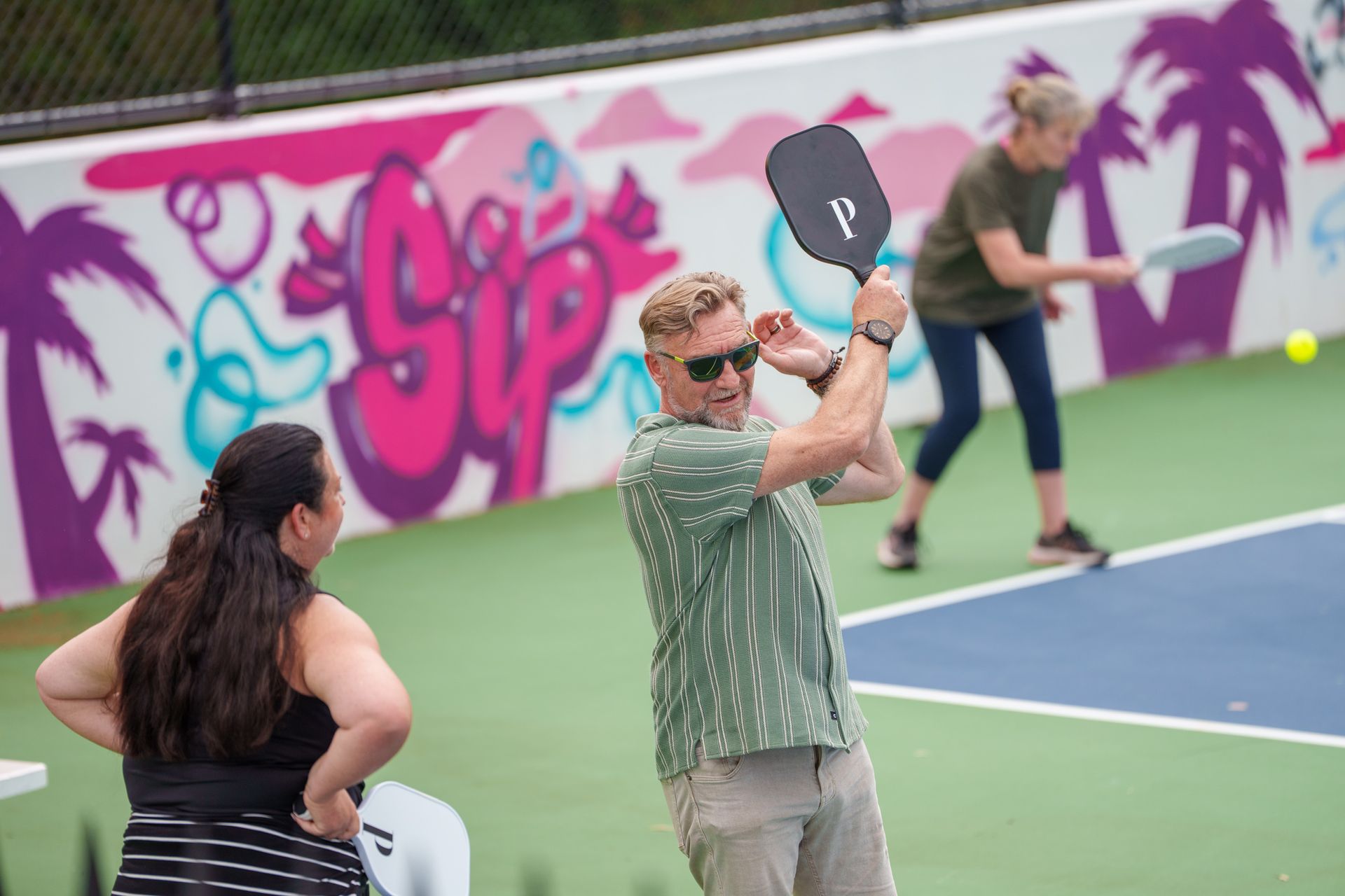 Group enjoying a lively pickleball session on colourful mural-lined outdoor courts