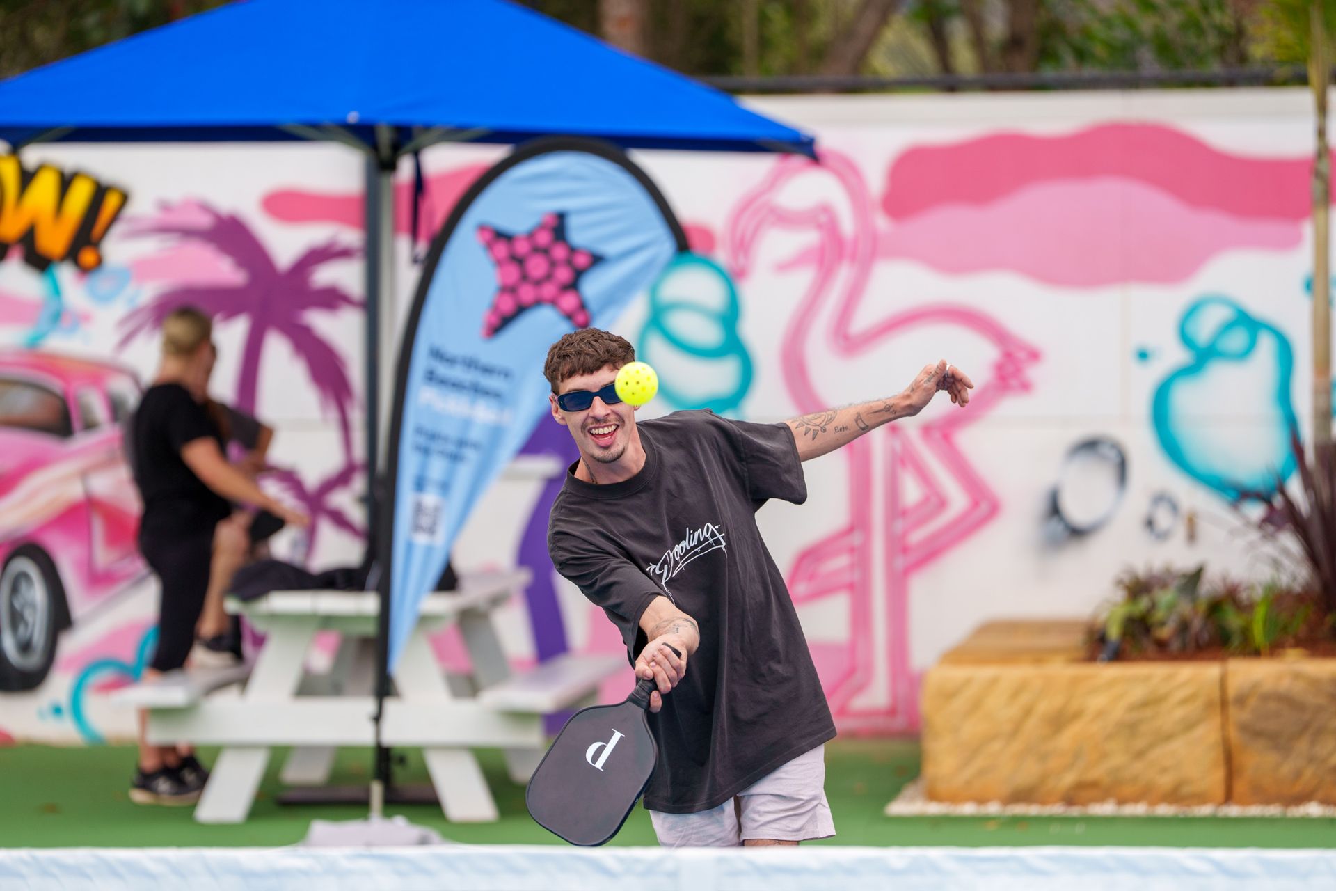 Man playing pickleball on an outdoor court beside vibrant mural artwork
