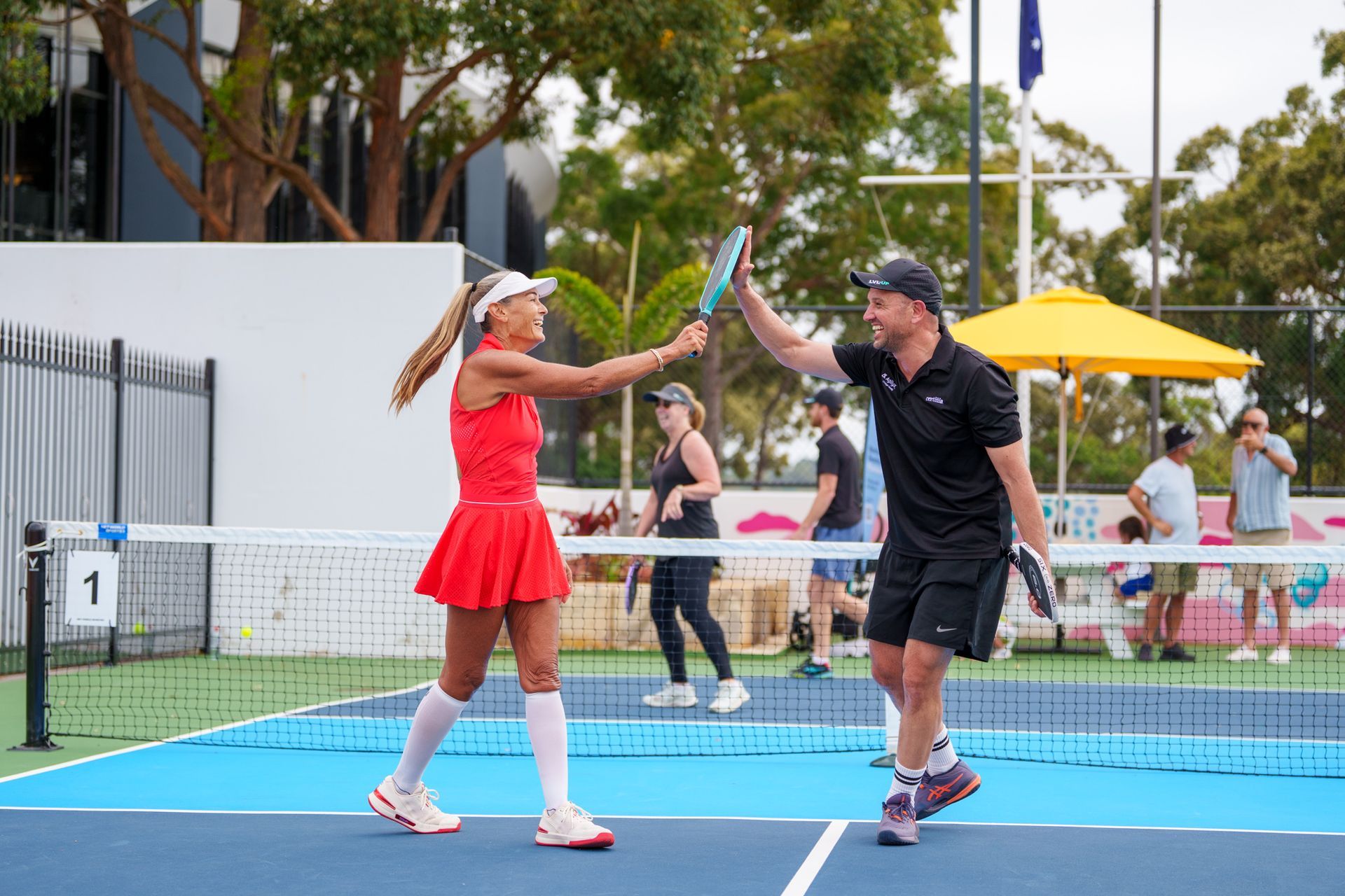 Two pickleball players high-fiving during an outdoor match on community courts