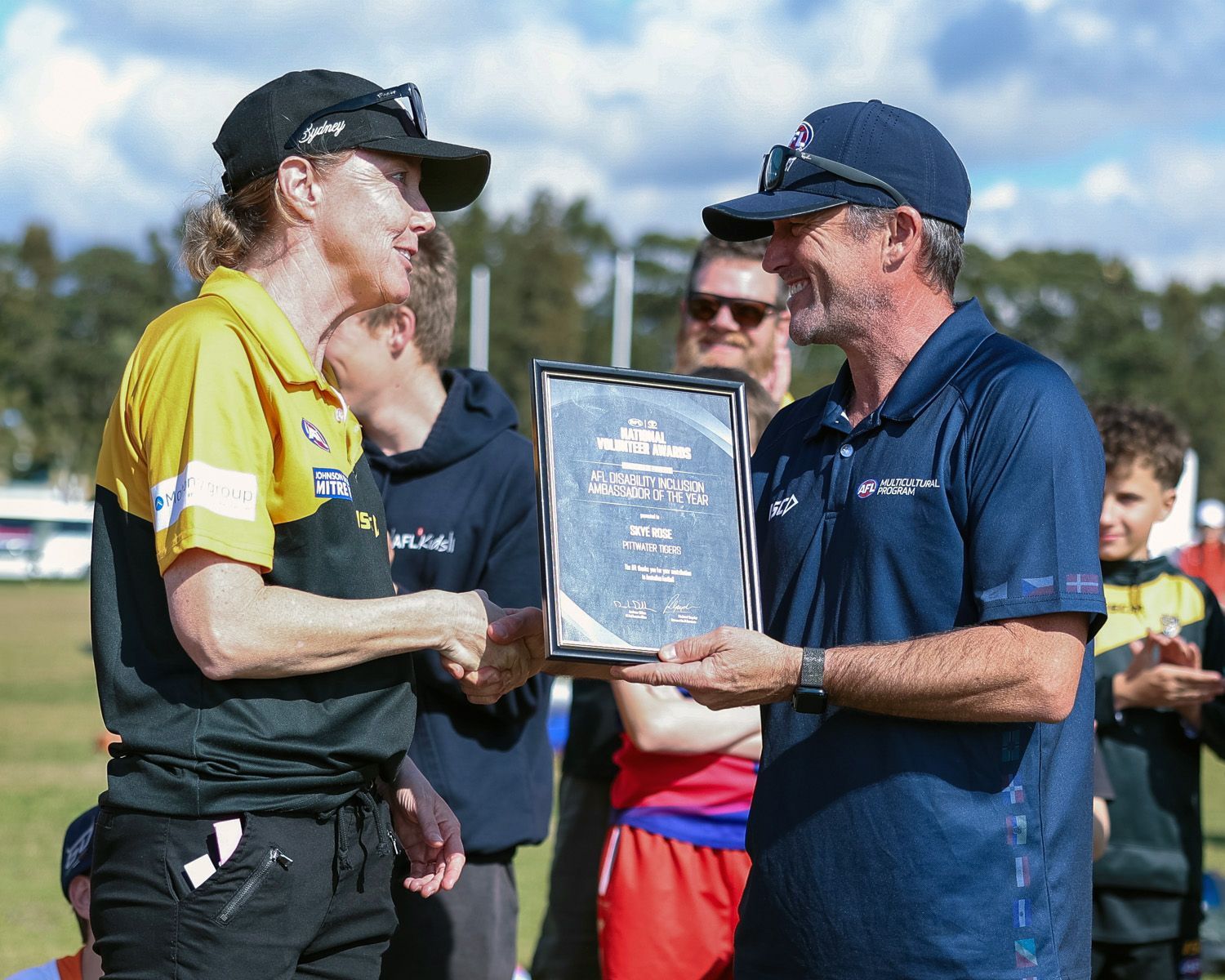 Two men exchanging a framed award during an outdoor sports community gala