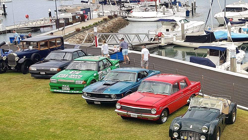 Classic cars parked on grass near a marina during a Pittwater motor club event