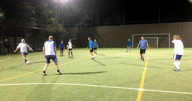 Players enjoying social football on a lit outdoor court during evening play