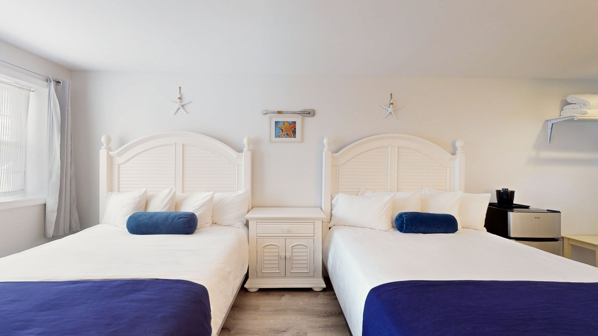 A hotel room with two beds and two nightstands.