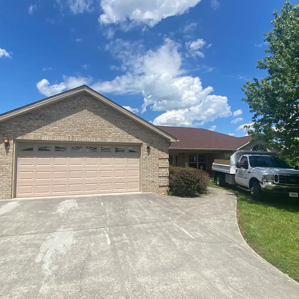 A tan brick house with a two-car garage and a truck parked in the driveway on a sunny day.