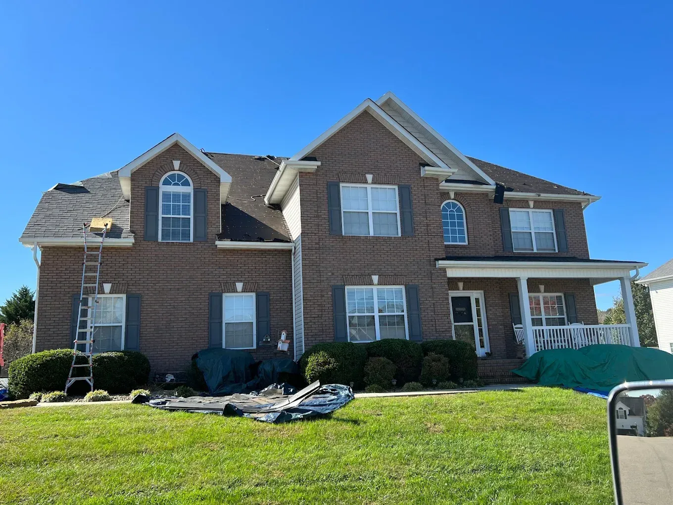 Two-story brick house with ladder on roof, green grass, and a clear blue sky.