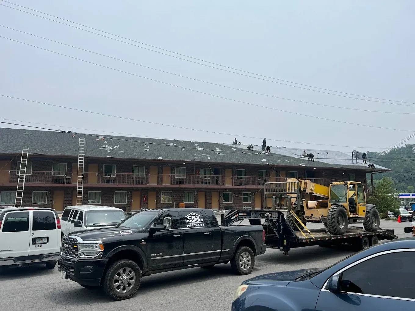 Black truck hauling yellow construction equipment on a trailer; motel in background.